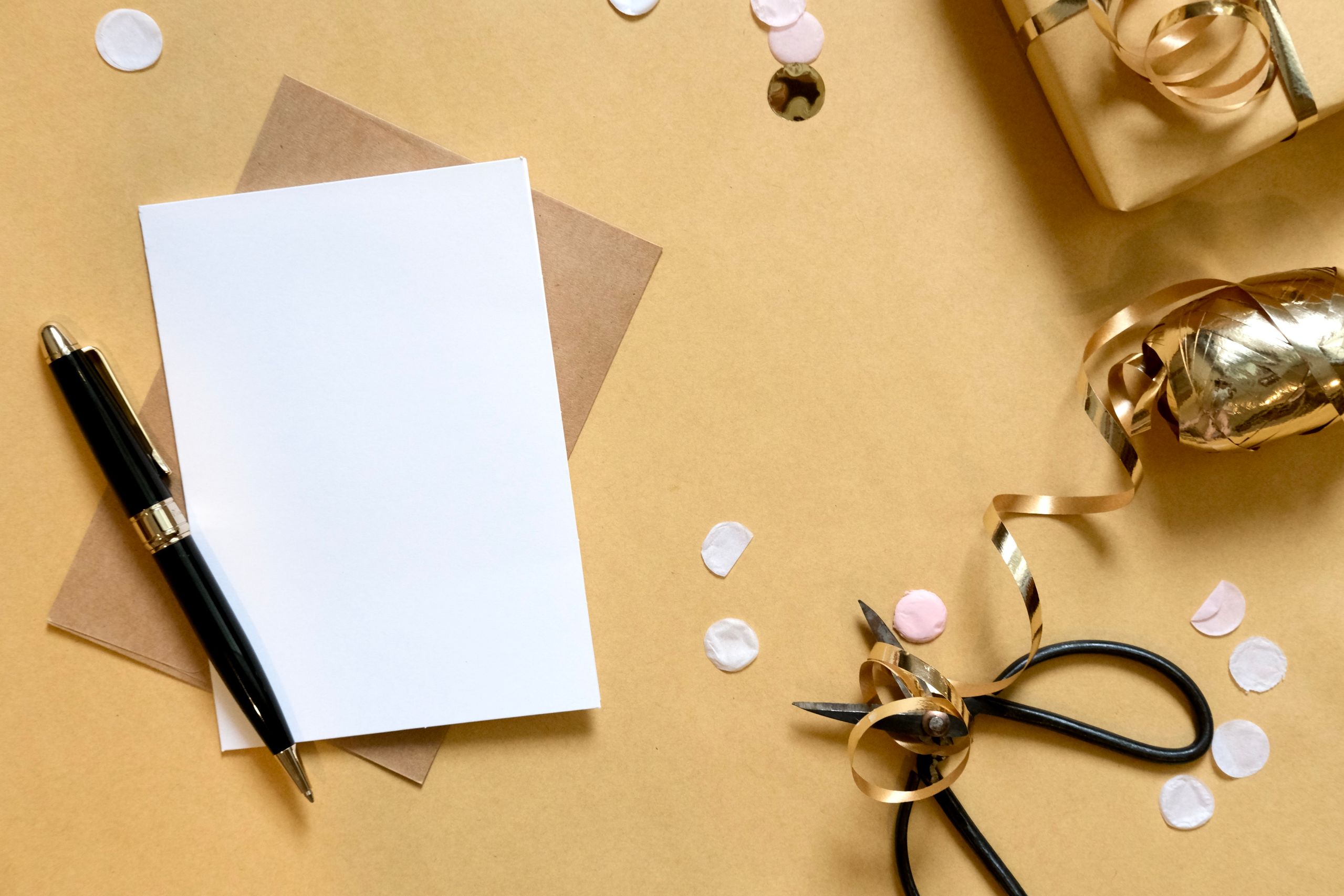 Stack of stationery, green notebook, floral card, gold pen, ribbon
